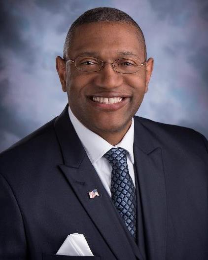 Dr. Ardrelle Evans is wearing a blue suit and tie with American flag pin